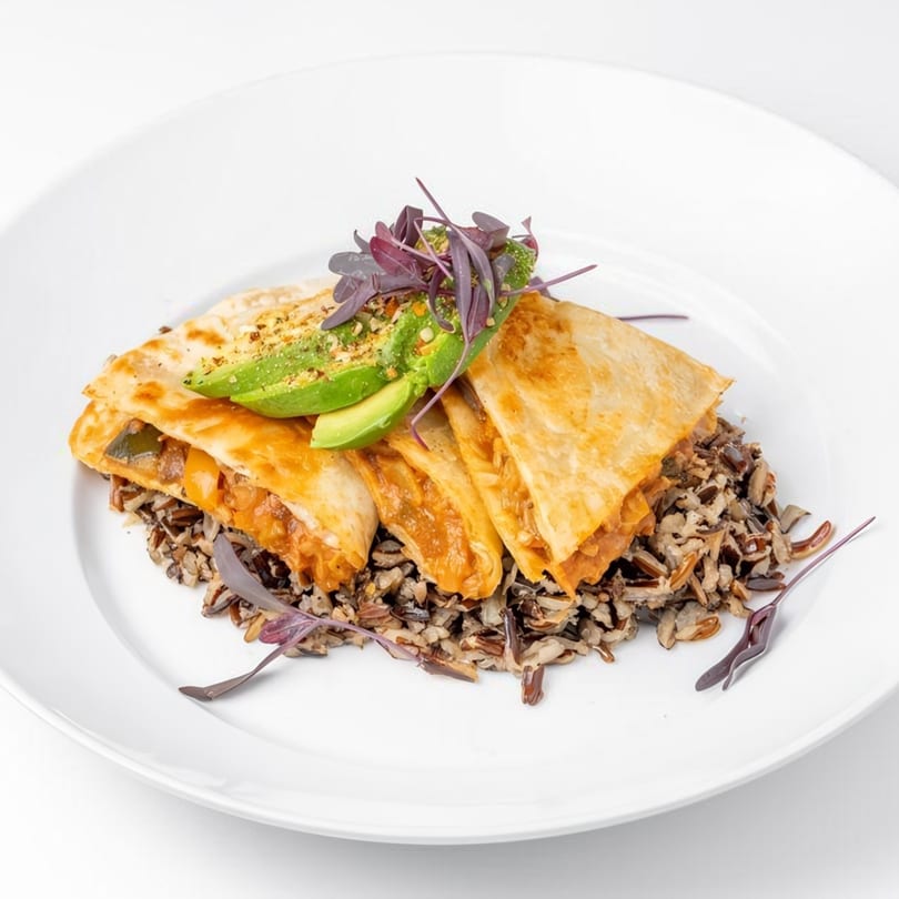 Golden quesadillas with avocado and purple microgreens, served over wild rice on a white plate.
